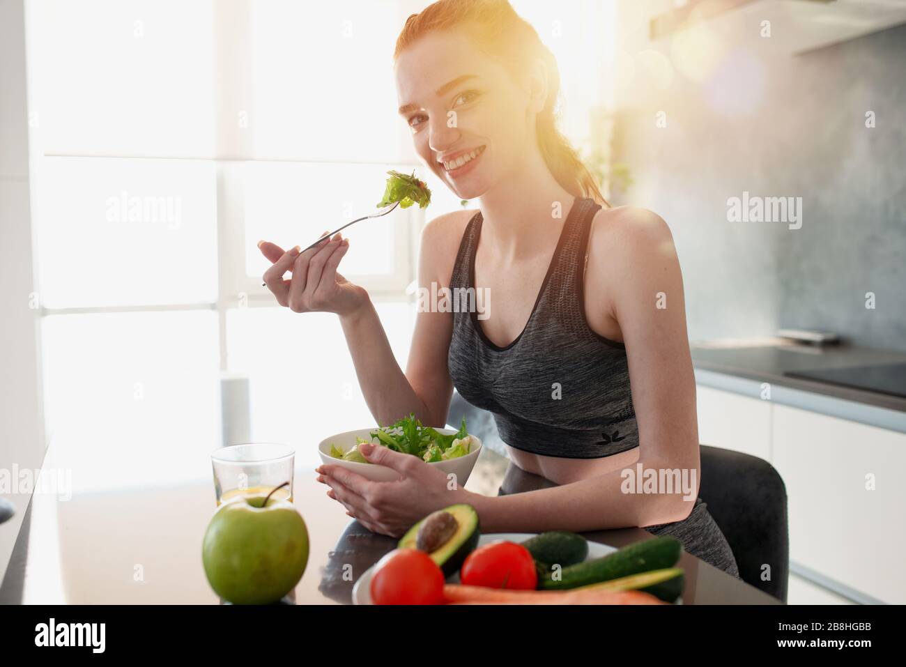 Sportliches Mädchen mit Turnhallenkleidung isst Salat in der Küche Stockfoto