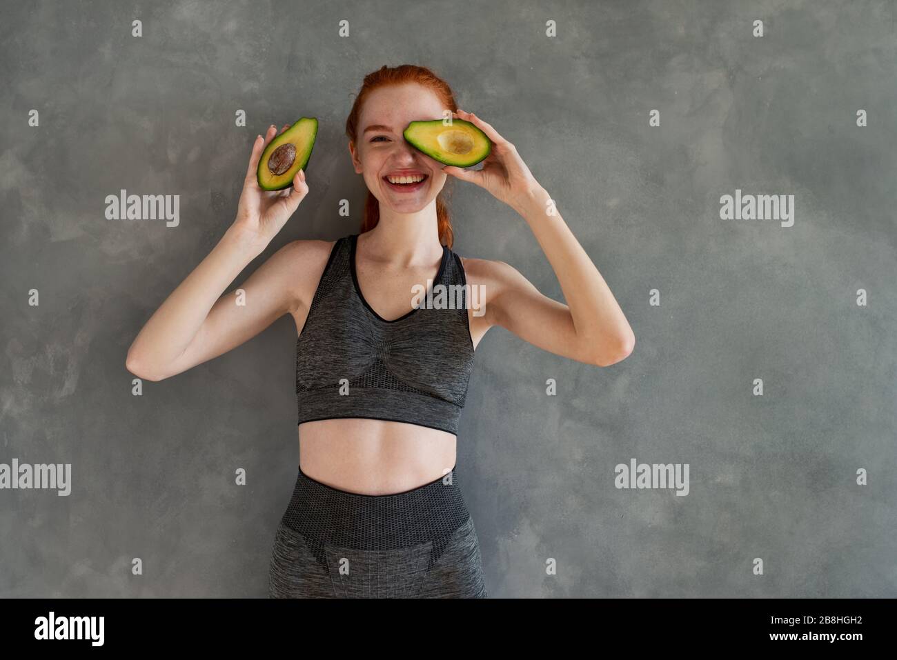 Sportliches Mädchen mit Turnhallenkleidung isst zu Hause Avocado Stockfoto