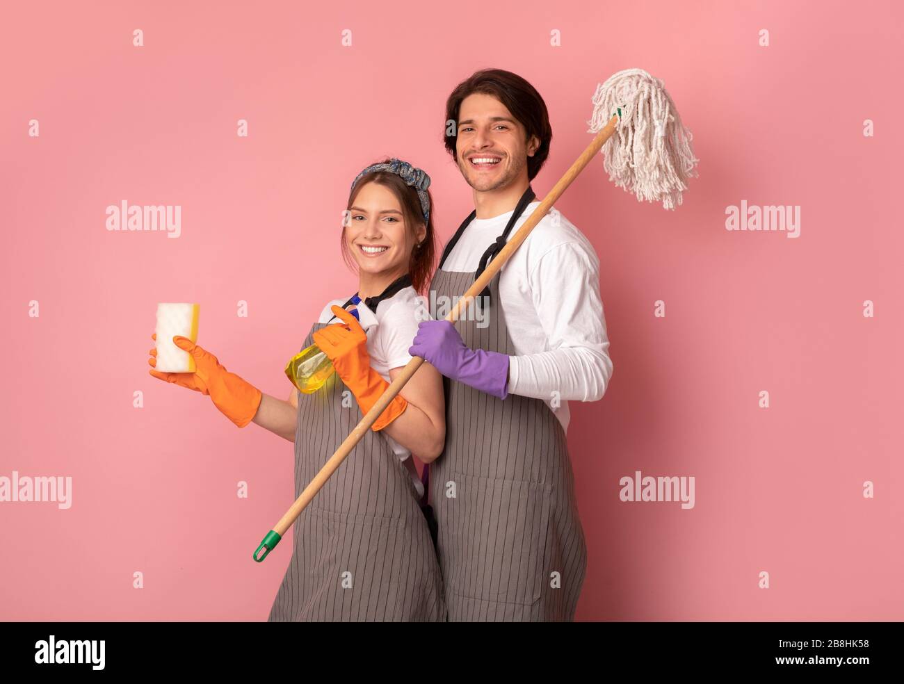 Reinigungsservice in Schürzen, die über rosafarbenem Hintergrund im Studio posieren Stockfoto