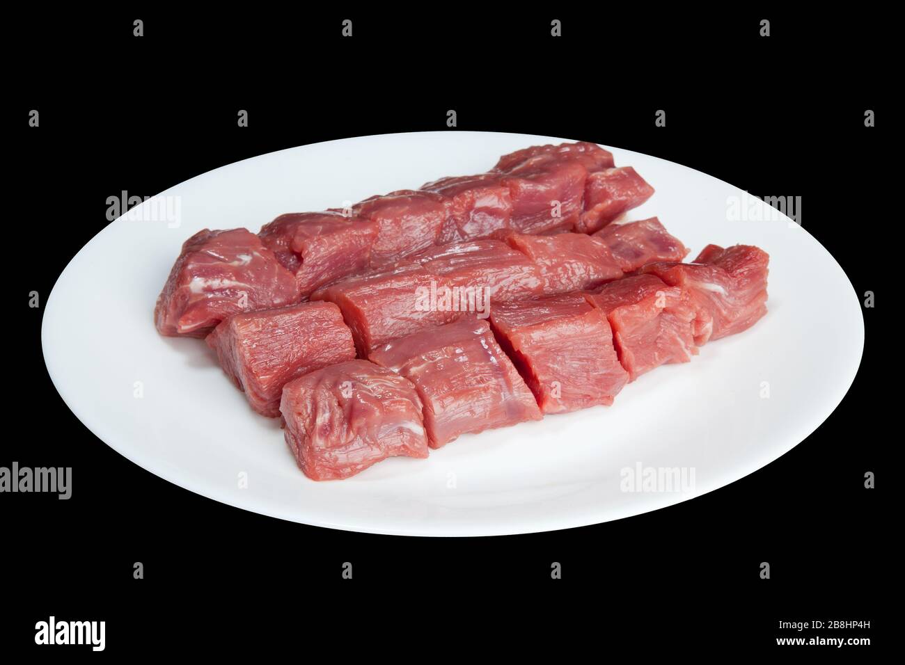 Stücke rohes Fleisch auf einer weißen Platte sind auf schwarzem Grund isoliert Stockfoto