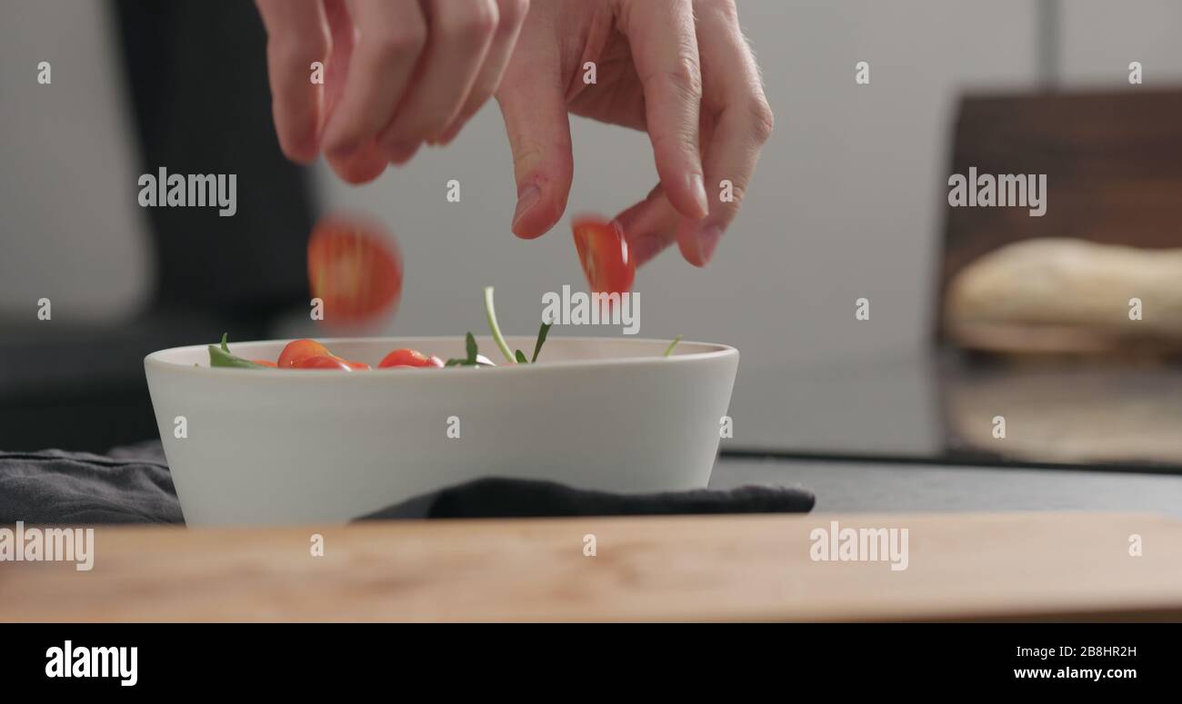Mann hinzufügen Tomatenhälften in weiße Schüssel, um einen Salat, breite Foto zu machen Stockfoto