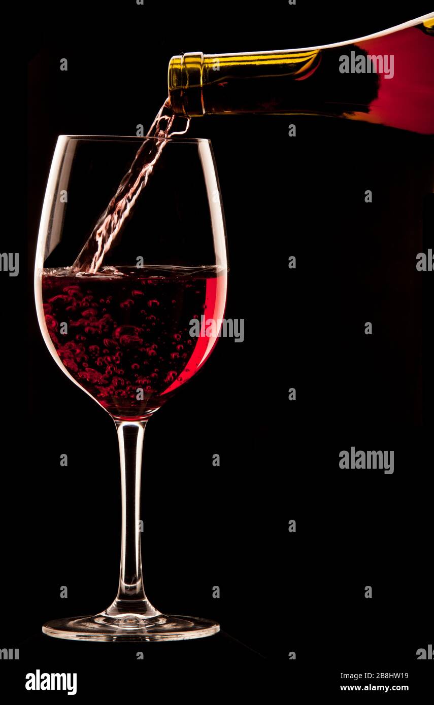 Ein Glas Rotwein auf schwarzem Hintergrund gießen. Stockfoto