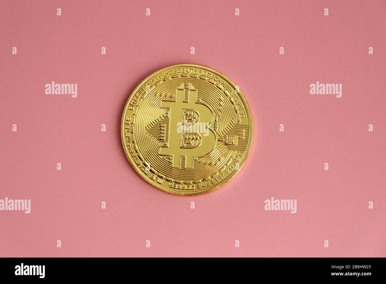 Goldmünze mit dem Bild von Bitcoin liegt auf einem rosafarbenen Hintergrund. Stockfoto