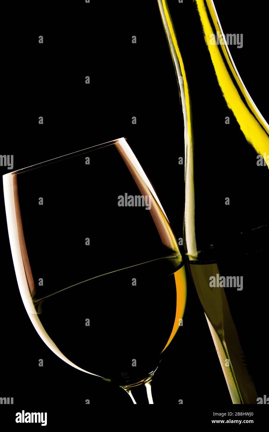 Hintergrundbeleuchtete Details eines Glasweins und der Weinflasche vor einem einfarbigen schwarzen Hintergrund. Stockfoto
