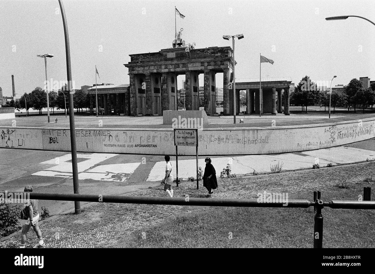 Menschen, die an einem Abschnitt der Berliner Mauer am Brandenburger Tor vorbeilaufen, von der westlichen Seite der Kluft aus gesehen. Die Berliner Mauer war eine von der Deutschen Demokratischen Republik (DDR, Ostdeutschland) am 13. August 1961 errichtete Barriere, die West-Berlin von der umliegenden DDR und von Ost-Berlin völlig abgrenzte. Die Mauer wurde am 9. November 1989 die freie Personenbewegung von Ost nach West erlaubt. Stockfoto