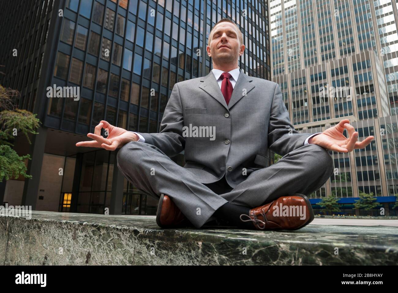 Ruhiger Geschäftsmann, der draußen vor der Skyline der Stadt meditiert Stockfoto