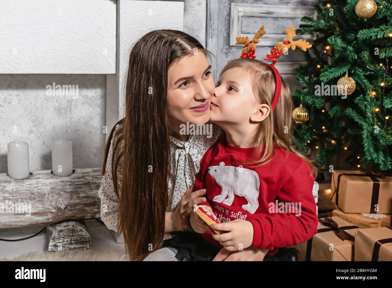 Kleines Mädchen küsst ihre Mutter auf dem weihnachtsfoto Stockfoto
