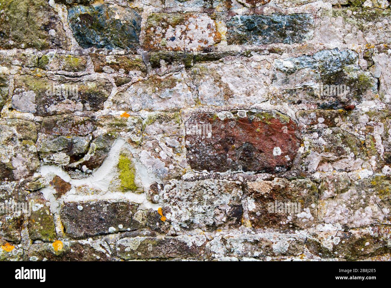 Steinwand mit unregelmäßig geformten Steinen verwittert und alt mit kleinen Flecken Moos Stockfoto