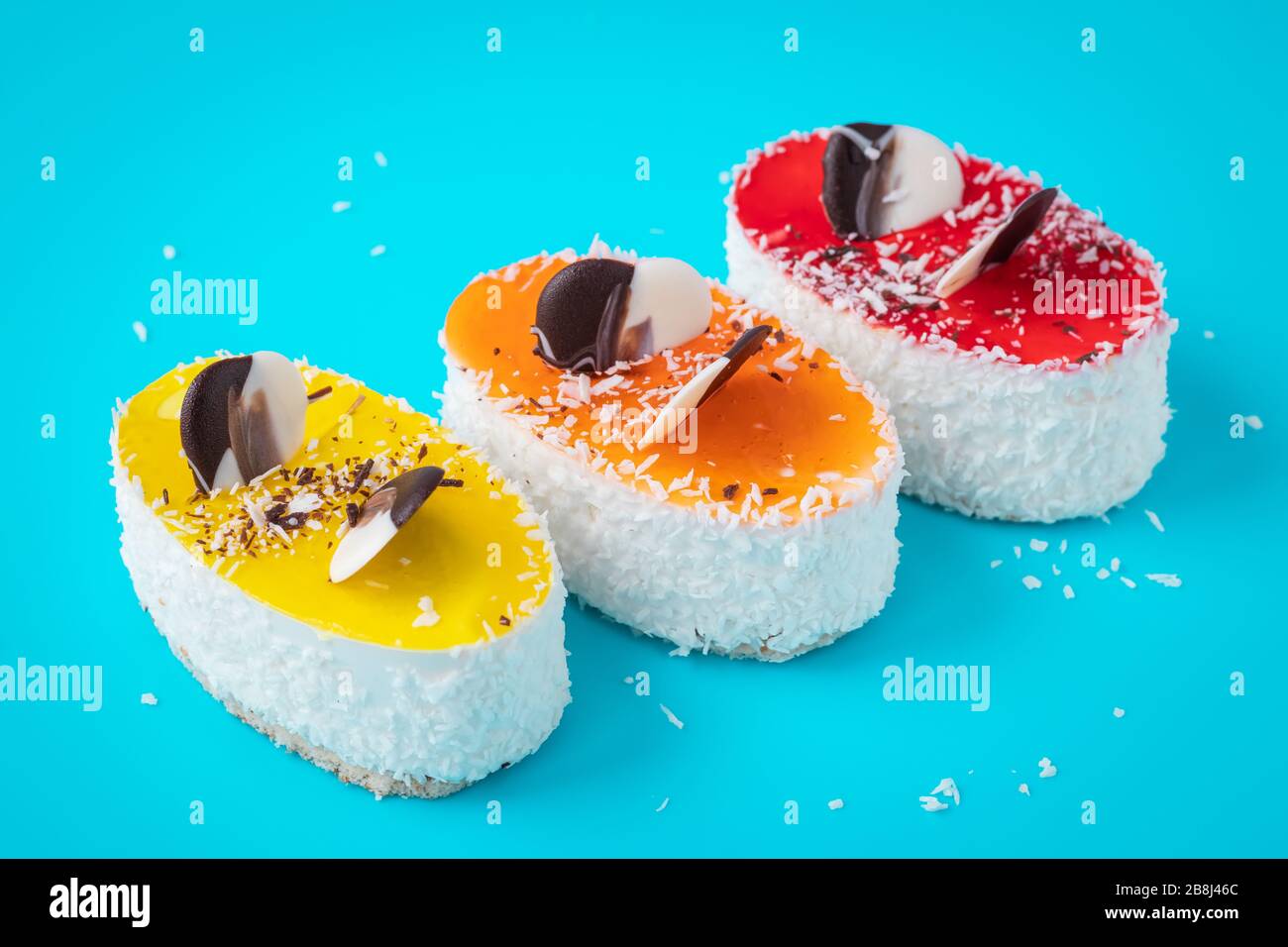 Kuchenstücke sind mit Kokosflocken verziert. Buntes Gebäck auf blauem Grund. Hausgemachtes, buntes Dessert Stockfoto