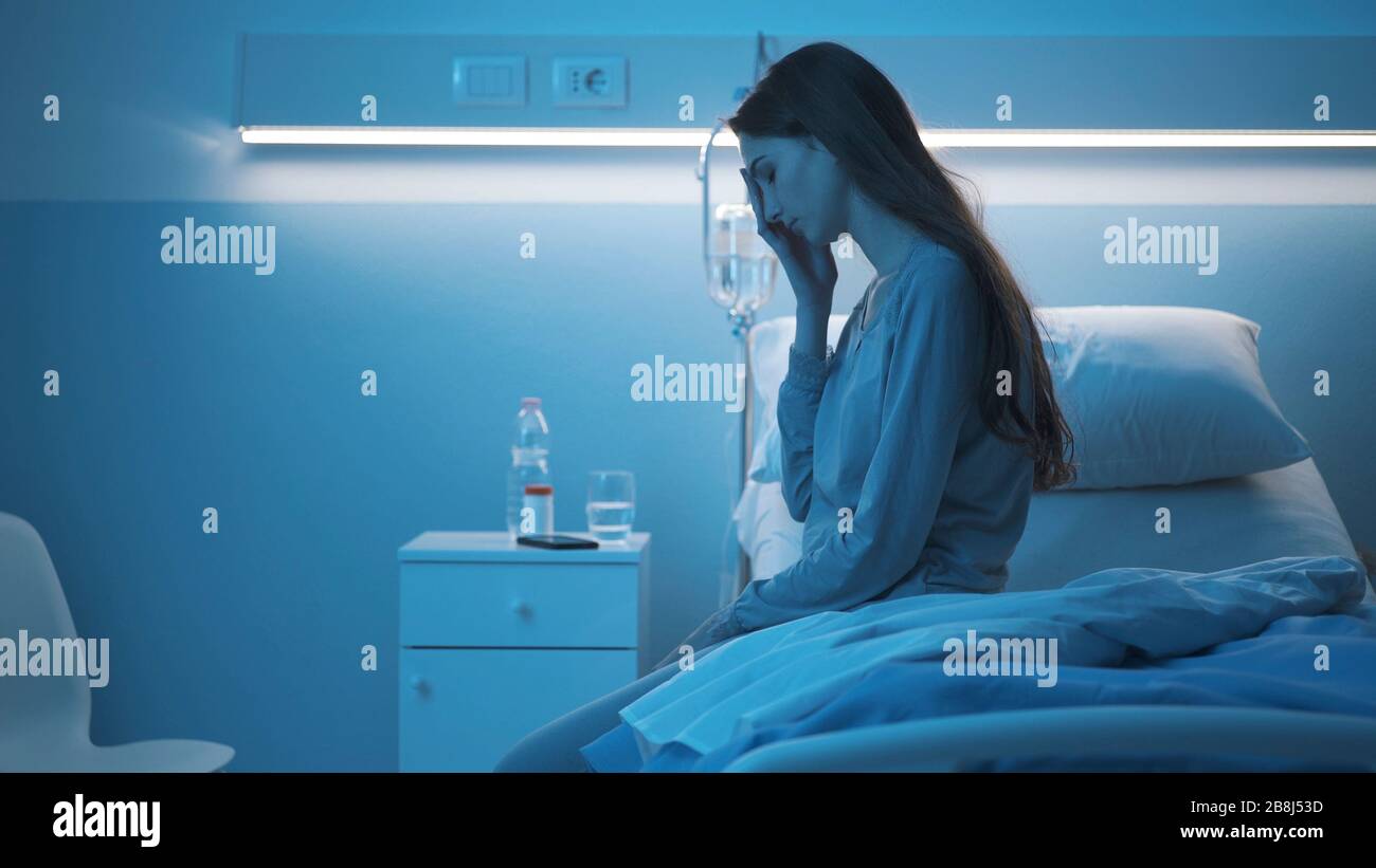 Schlaflose Frau, die spät in der Nacht auf dem Krankenbett sitzt, ist besorgt und traurig Stockfoto