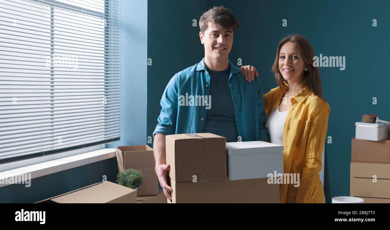 Fröhliches junges Paar posiert in ihrem neuen Haus und hält Kartonboxen: Heimverlagerungskonzept Stockfoto