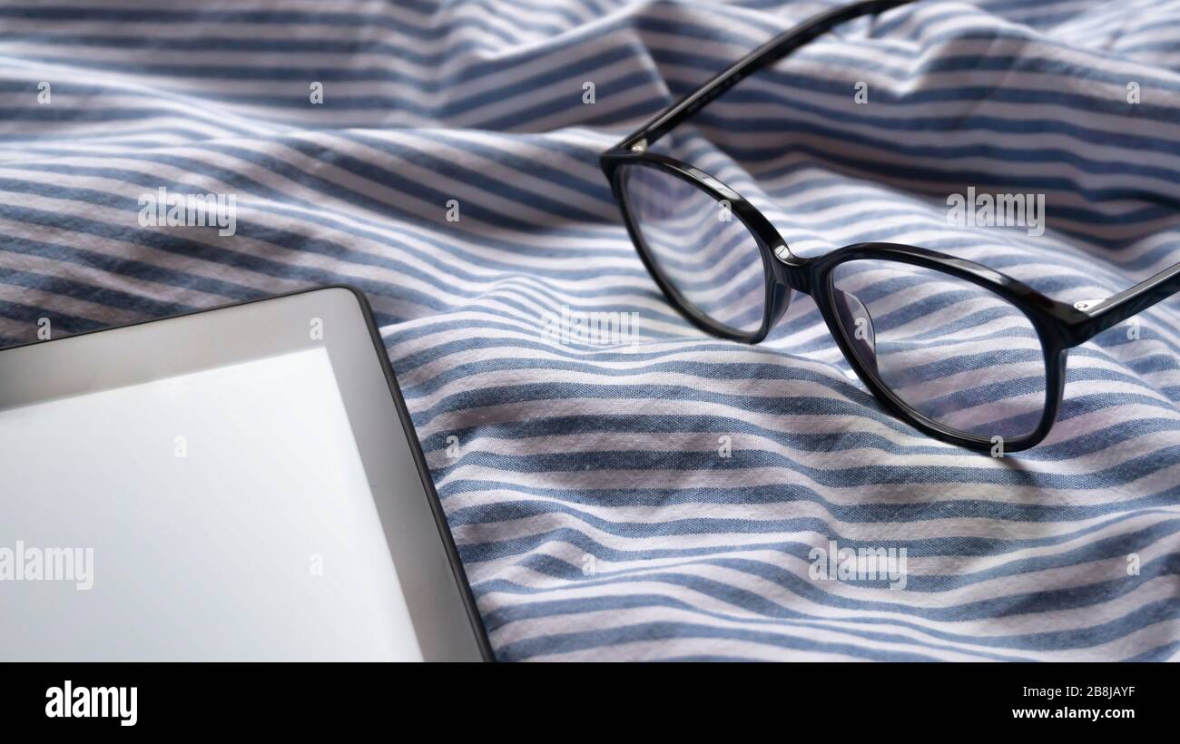 Editierbarer oder benutzerdefinierter E-Reader mit Brille im Hintergrund auf dem Bett an einem sonnigen, ruhigen Morgen Stockfoto