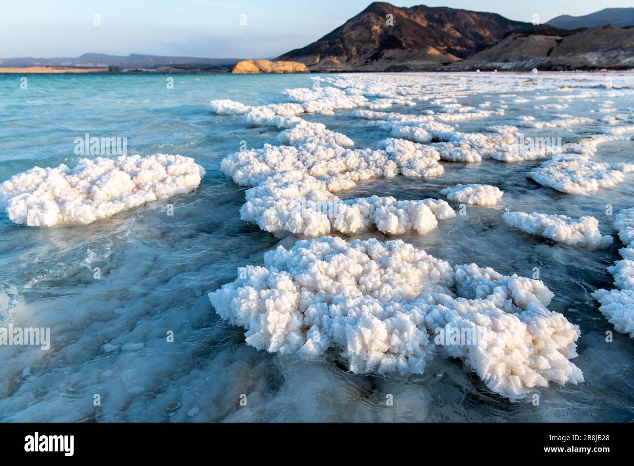 Afrika, Dschibuti, Assalsee. Aus dem Wasser aufkommende Salzkristalle mit Bergen im Hintergrund Stockfoto