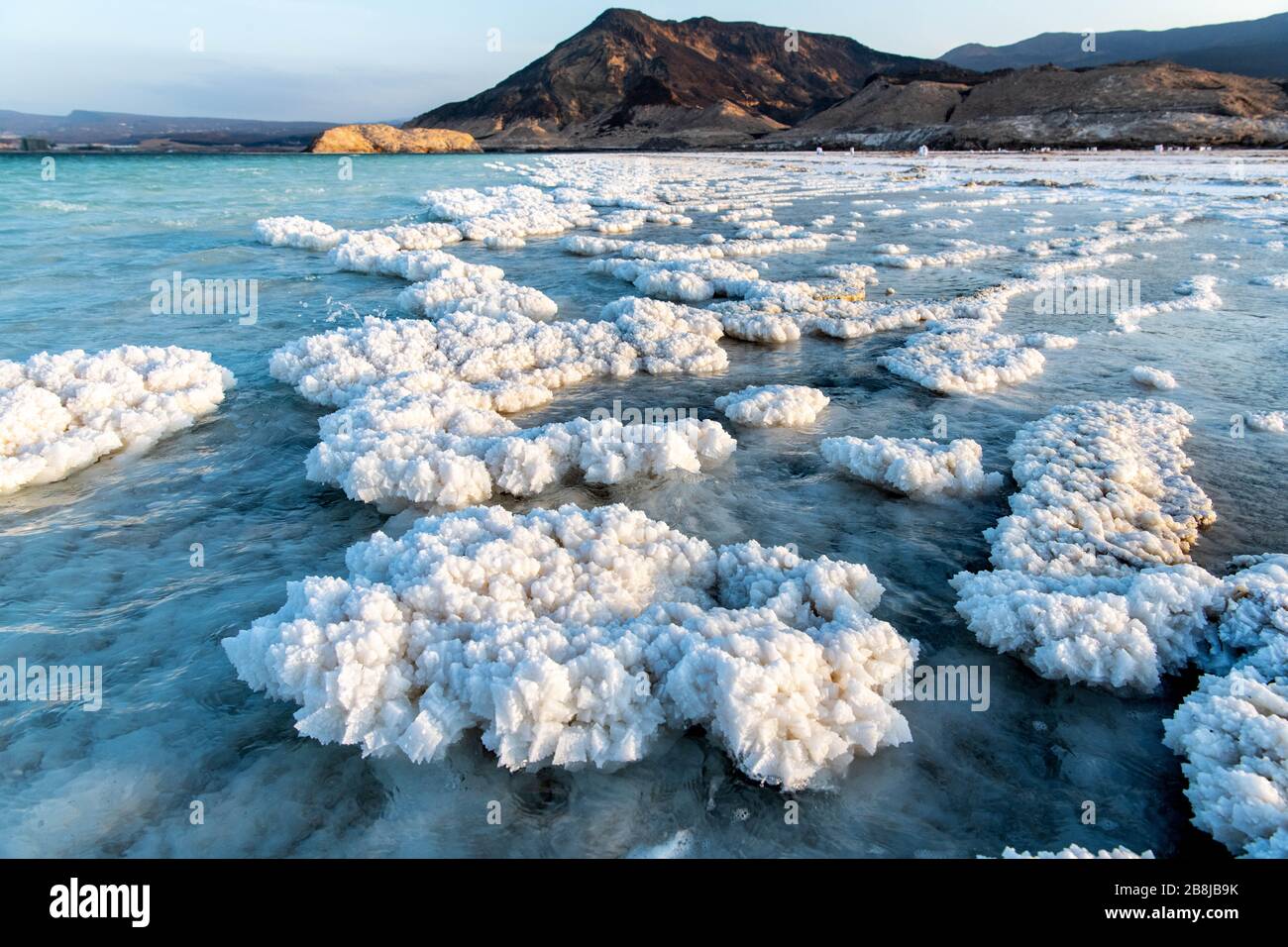 Afrika, Dschibuti, Assalsee. Aus dem Wasser aufkommende Salzkristalle mit Bergen im Hintergrund Stockfoto