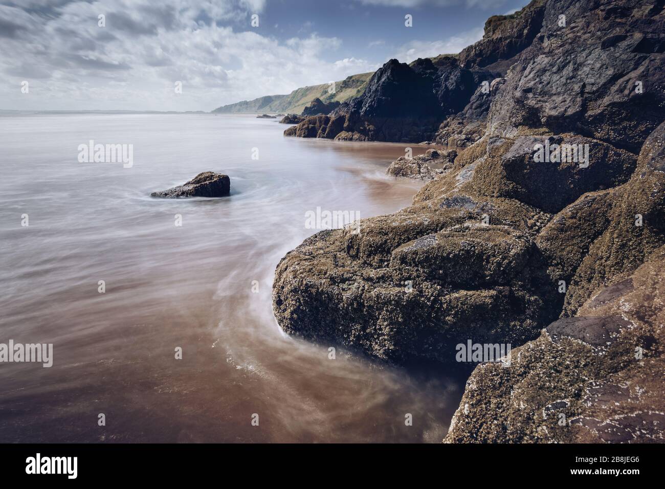 Blick auf St Cyrus Beach in Angus, Schottland an einem sonnigen Tag, Sand und Felsen im Vordergrund sichtbar Blick entlang der Küste in die Ferne. Stockfoto