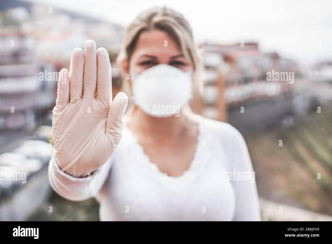 Junge Frau, die Gesichtsmaske und Latexhandschuhe trägt und gleichzeitig eine Stopphandgeste zur Vorbeugung von Coronavirus zeigt - Stop Spreading Covid 19 Concept - Focus o Stockfoto