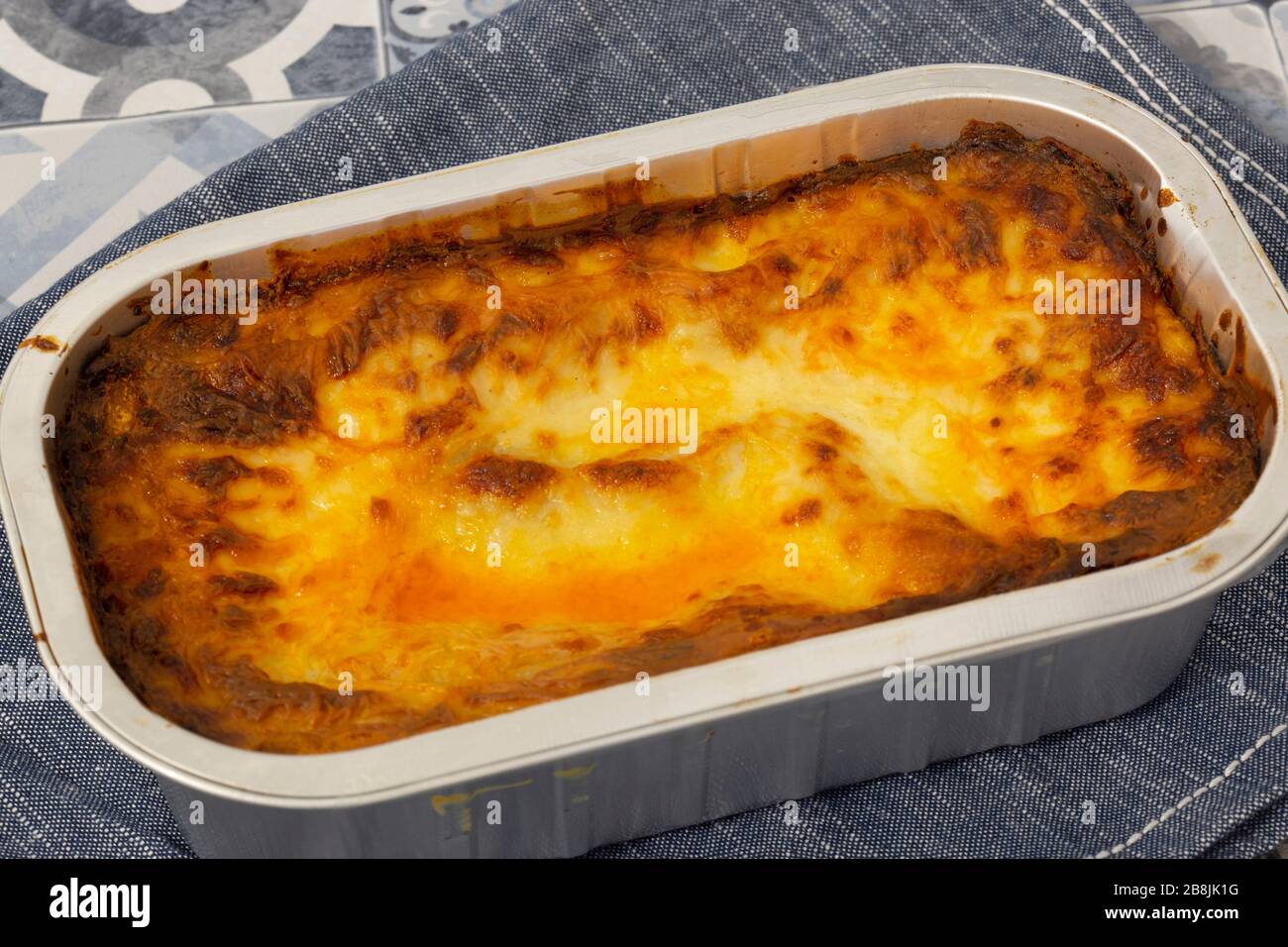 Beef Lasagne oder Lasagne zubereitete, tiefgefrorene Mahlzeit, die in einem Metallbackblech auf einem blauen Teehandel zubereitet wird. Fast-Food-Konzept Stockfoto