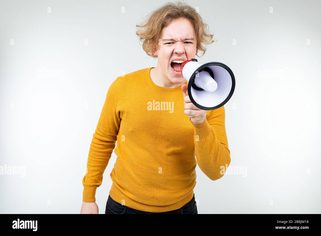 Blonder, gewellter Mann, der in einem Megafon auf weißem Studiohintergrund Nachrichten schreit Stockfoto