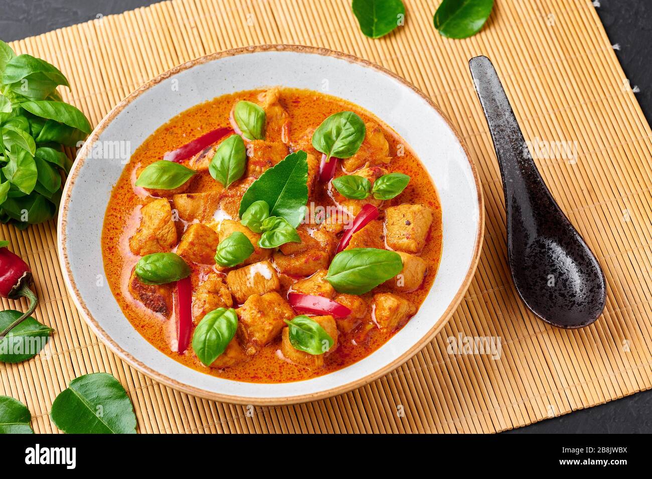 Thailändisches Panang Chicken Curry in weißer Platte mit schwarzem Schieferhintergrund. Phanaeng Curry ist ein thailändisches Gericht mit Huhn, Kaffir-Kalkblättern, roter Curry sa Stockfoto