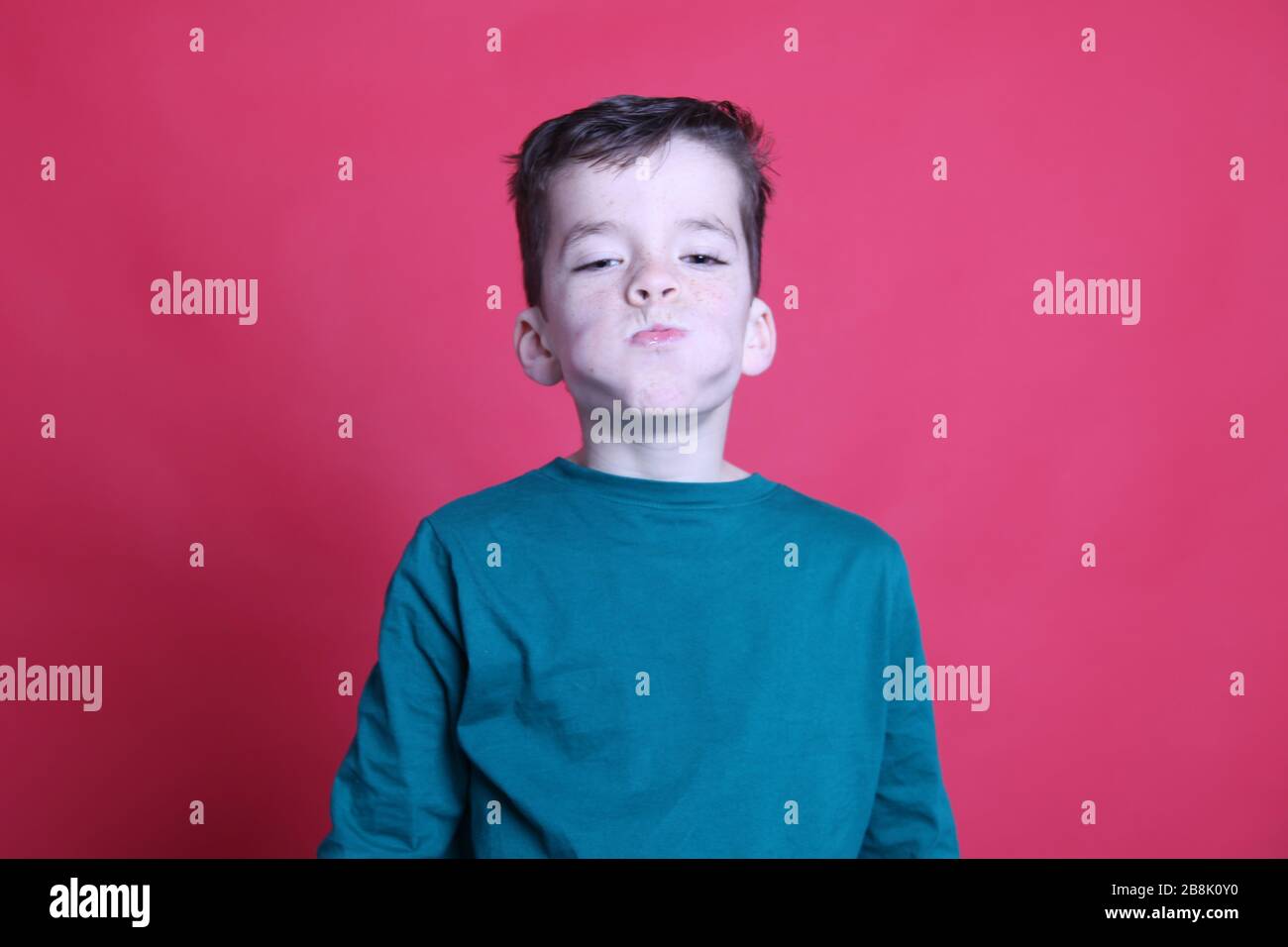 UK 8-jähriger Junge mit seinem Mund voller Orange, Wangen wulstig, roter Hintergrund, UK 2020 Stockfoto