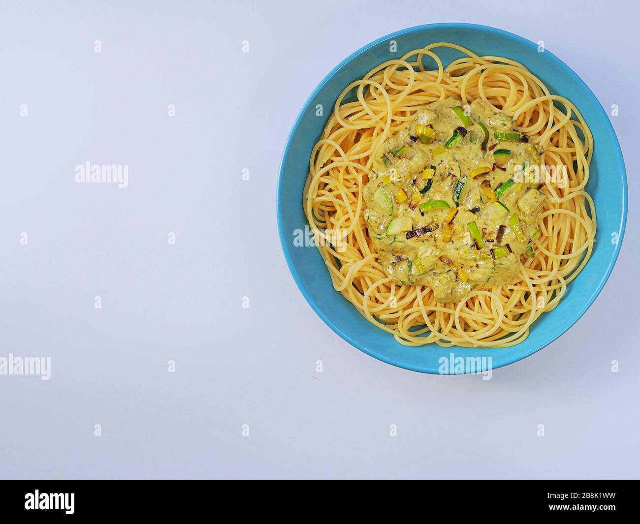 Spaghetti mit einer cremefarbenen Sauce mit Zucchini und Lauch in hellblauer Platte auf weißem Grund von oben. Stockfoto