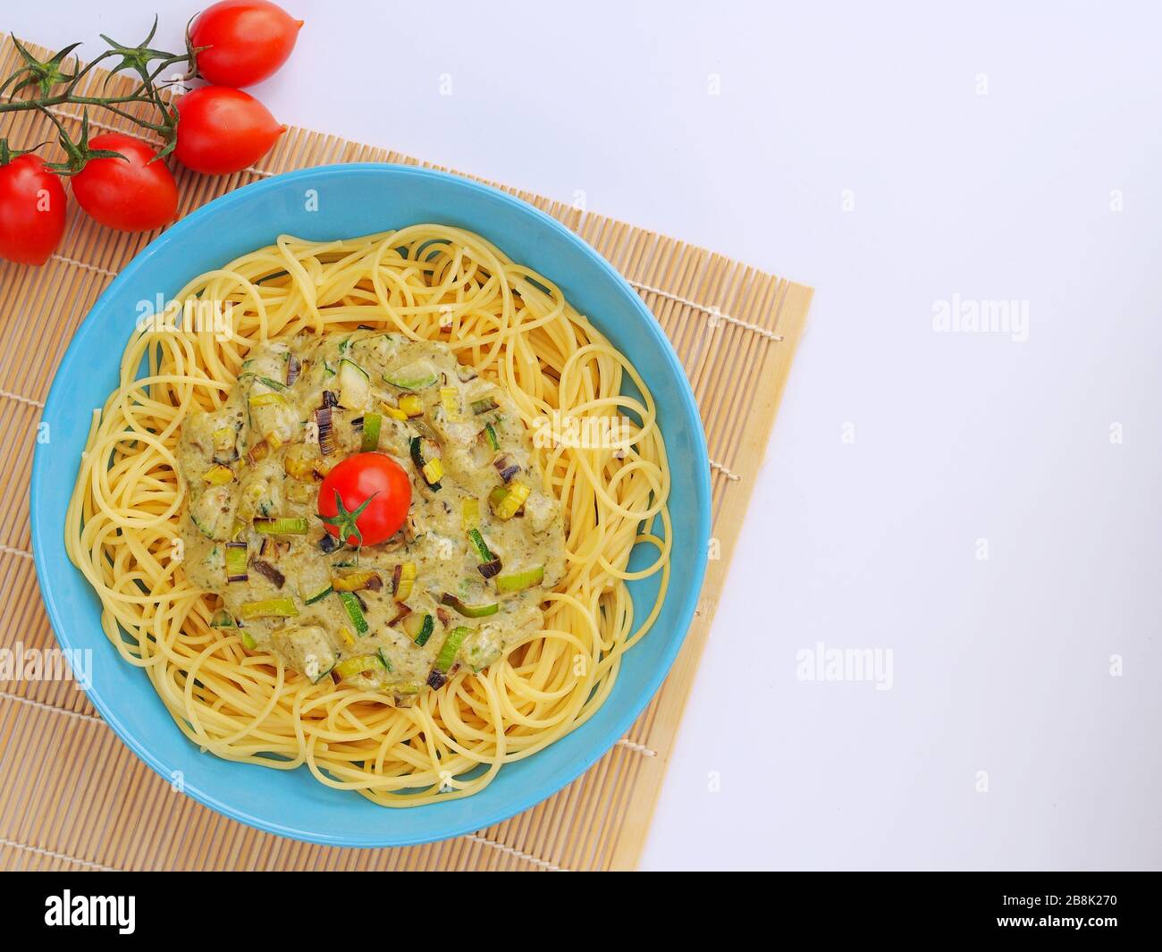 Spaghetti mit einer cremefarbenen Sauce mit Zucchini und Lauch in hellblauer Platte auf weißem Grund von oben. Stockfoto