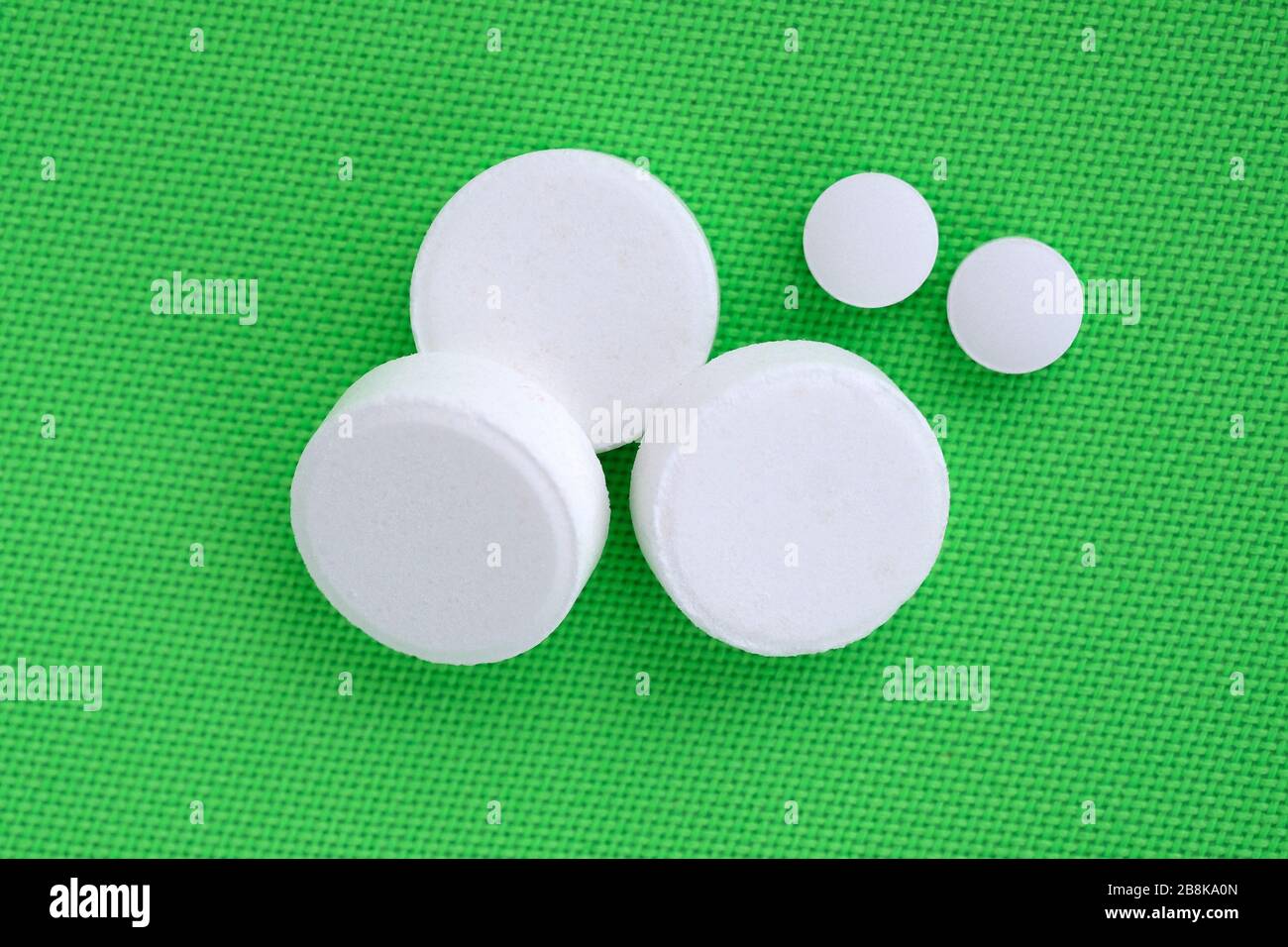 Drei große weiße Pillen und zwei kleine Pillen auf grünem Hintergrund. Weiße Pillen unterschiedlicher Größe werden von oben angezeigt. Runde Pillen, Medikamente. Stockfoto