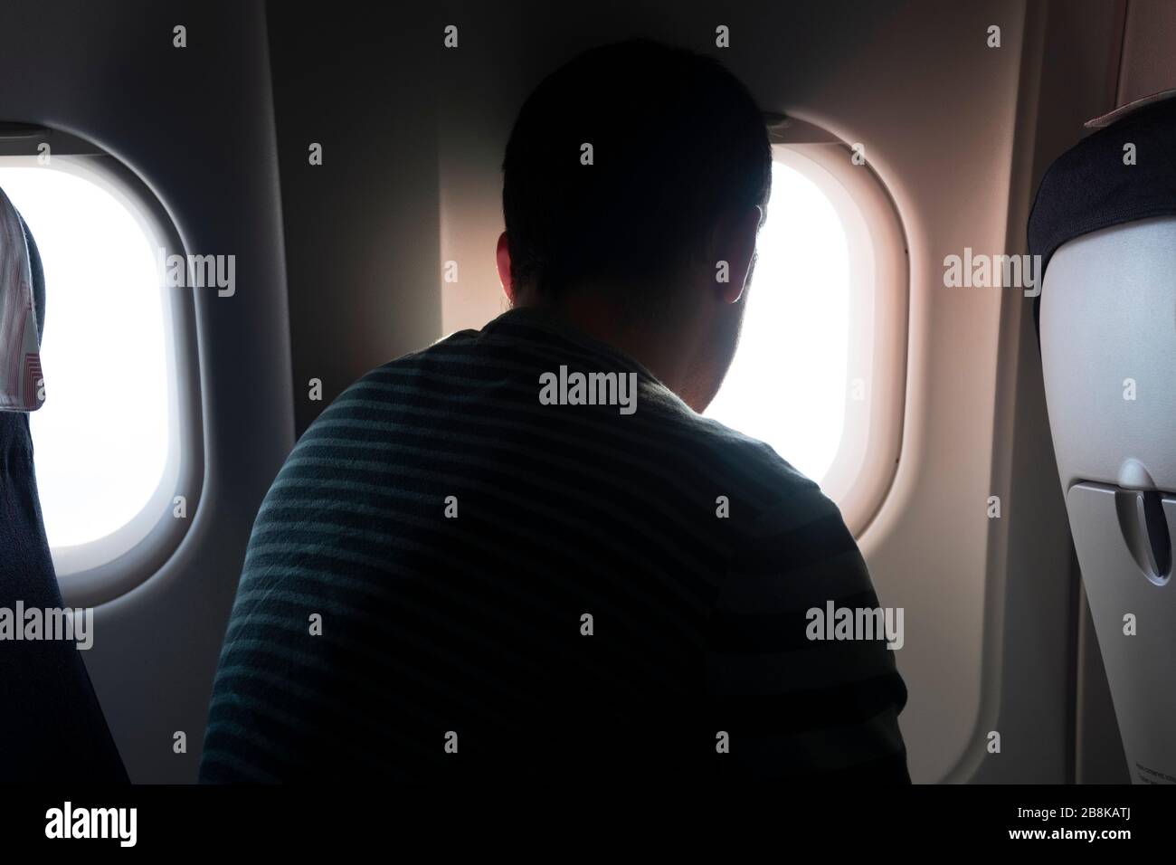 Eine Rückansicht eines Mannes, der in einem Flugzeug sitzt und den Blick vom Flugzeugfenster aus betrachtet. Stockfoto