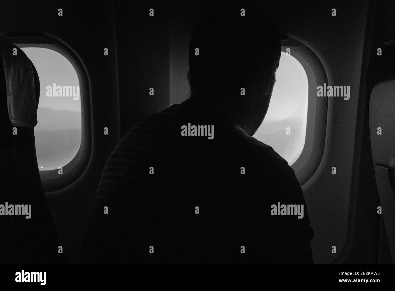 Eine Rückansicht eines Mannes, der in einem Flugzeug sitzt und den Blick vom Flugzeugfenster aus betrachtet. Stockfoto