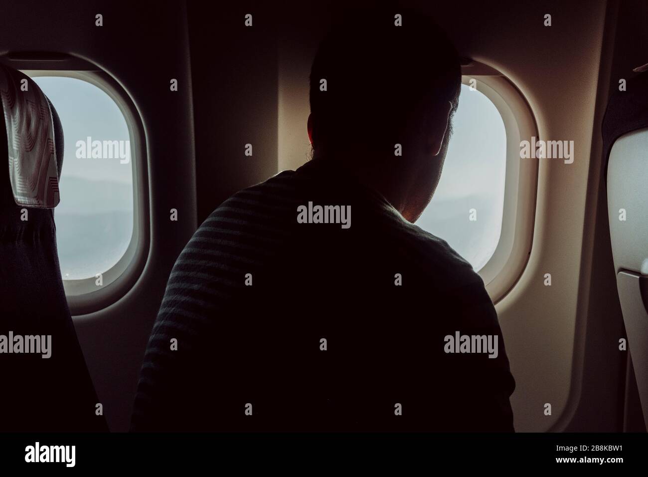 Eine Rückansicht eines Mannes, der in einem Flugzeug sitzt und den Blick vom Flugzeugfenster aus betrachtet. Stockfoto