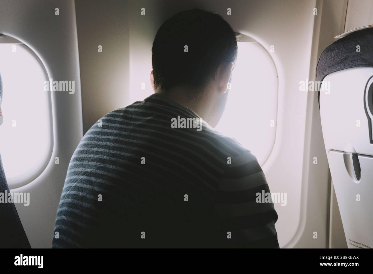 Eine Rückansicht eines Mannes, der in einem Flugzeug sitzt und den Blick vom Flugzeugfenster aus betrachtet. Stockfoto