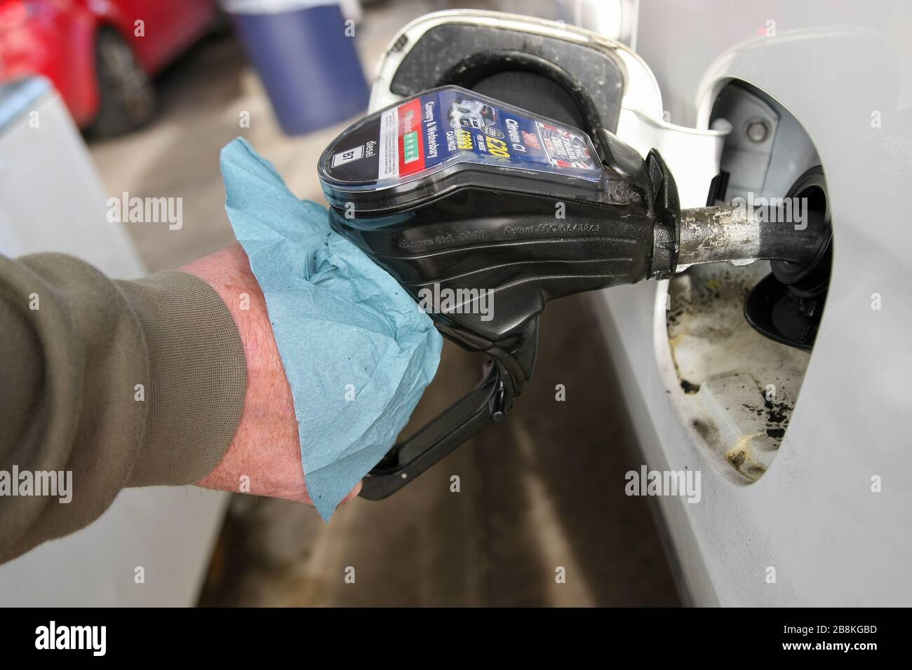 Birmingham, West Midlands, Großbritannien. März 2020. Tankstellen und Werkstätten fordern die Kunden auf, beim Befüllen ihrer Fahrzeuge Handschuhe zu tragen, da die Gefahr besteht, den COVID-19-Virus durch direkten Kontakt zu verbreiten. Dieser Kunde improvisiert mit frei verfügbaren Papiertüchern. Kredit: Peter Lopeman/Alamy Live News Stockfoto