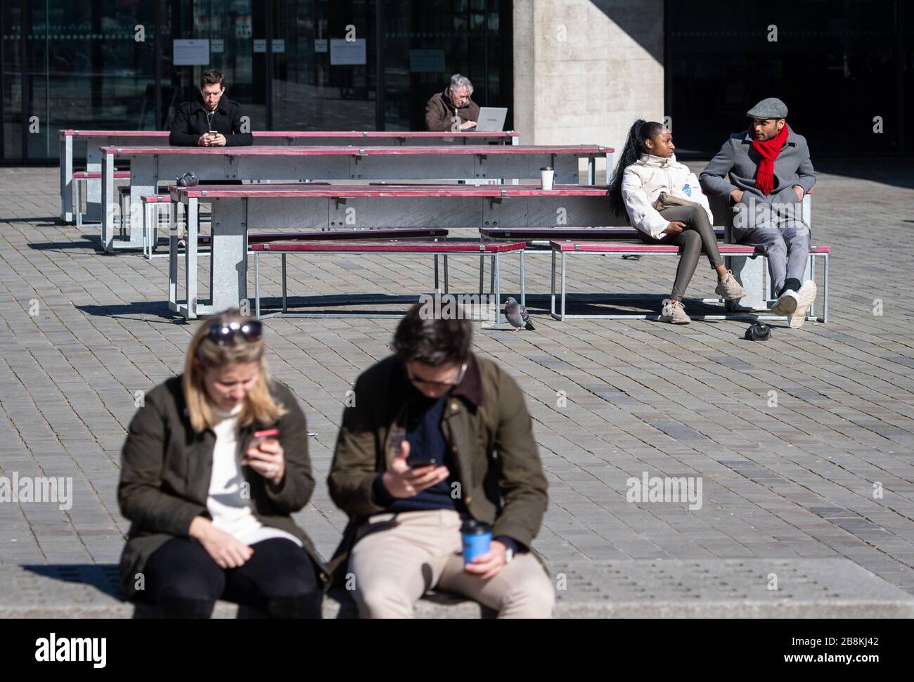 Die Menschen sitzen außerhalb des Nationaltheaters, auf der South Bank, im Zentrum Londons, nachdem Premierminister Boris Johnson die Schließung von Theatern, Pubs und Restaurants im ganzen Land angeordnet hatte, als die Regierung die Menschen dazu anregte, Ratschläge zur sozialen Distanzierung während des Coronavirus-Ausbruchs zu befolgen. Stockfoto