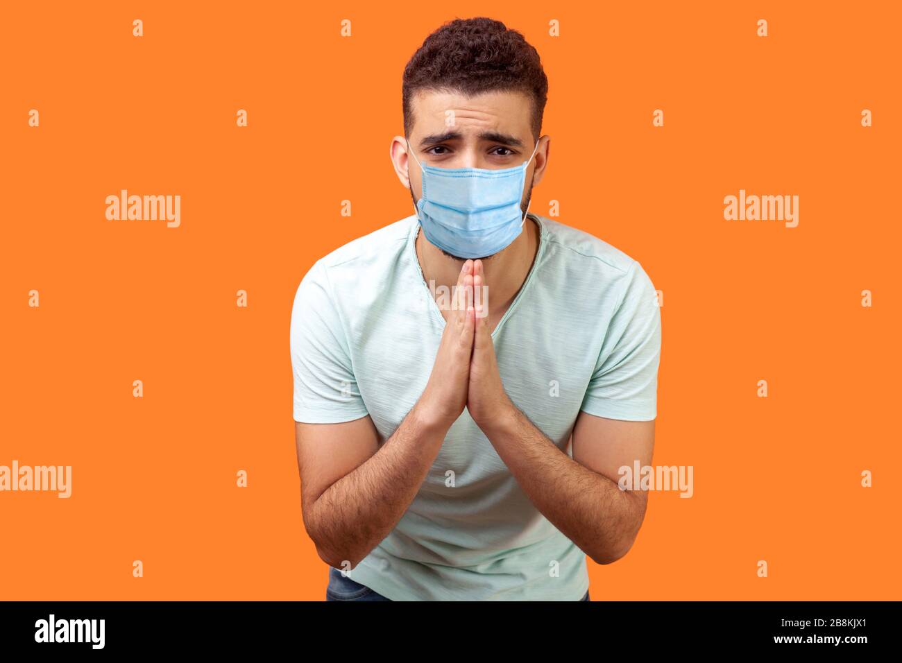 Bitte, ich bettele! Porträt des aufgebrachten Mannes mit medizinischer Maske in weißem T-Shirt, das die Arme im Gebet hält, Hilfe oder Vergebung mit andeutenden Augen bittet. Stockfoto