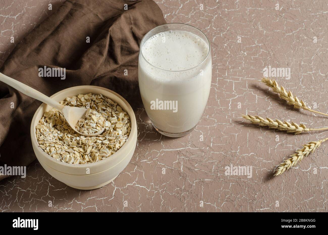 Hafermilch in einem Glas auf beigefarbenem Hintergrund mit Hafer, Pikeletten. Das Konzept des Veganismus, der Rohkost, des gesunden Essens. Richtiges Frühstück, Kinder m Stockfoto