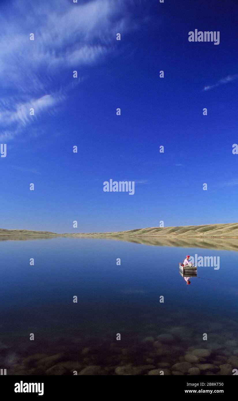 Ein Mann, der in einem Boot auf dem ruhigen Wasser des McGregor Lake, Alberta Canada, angeln kann Stockfoto