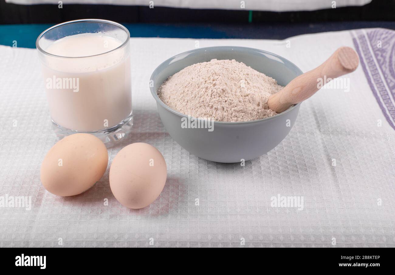 Ein Glas Milch mit rohen Eiern und eine Schüssel mit Allzweckmehl Stockfoto