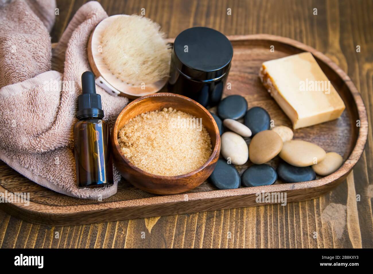 Spa Stillleben mit Massagesteinen, braunem Zuckerschrub, Körperöl und Pinsel, Baumwolltuch auf rustikalem Holztablett, Heim-SPA Stockfoto