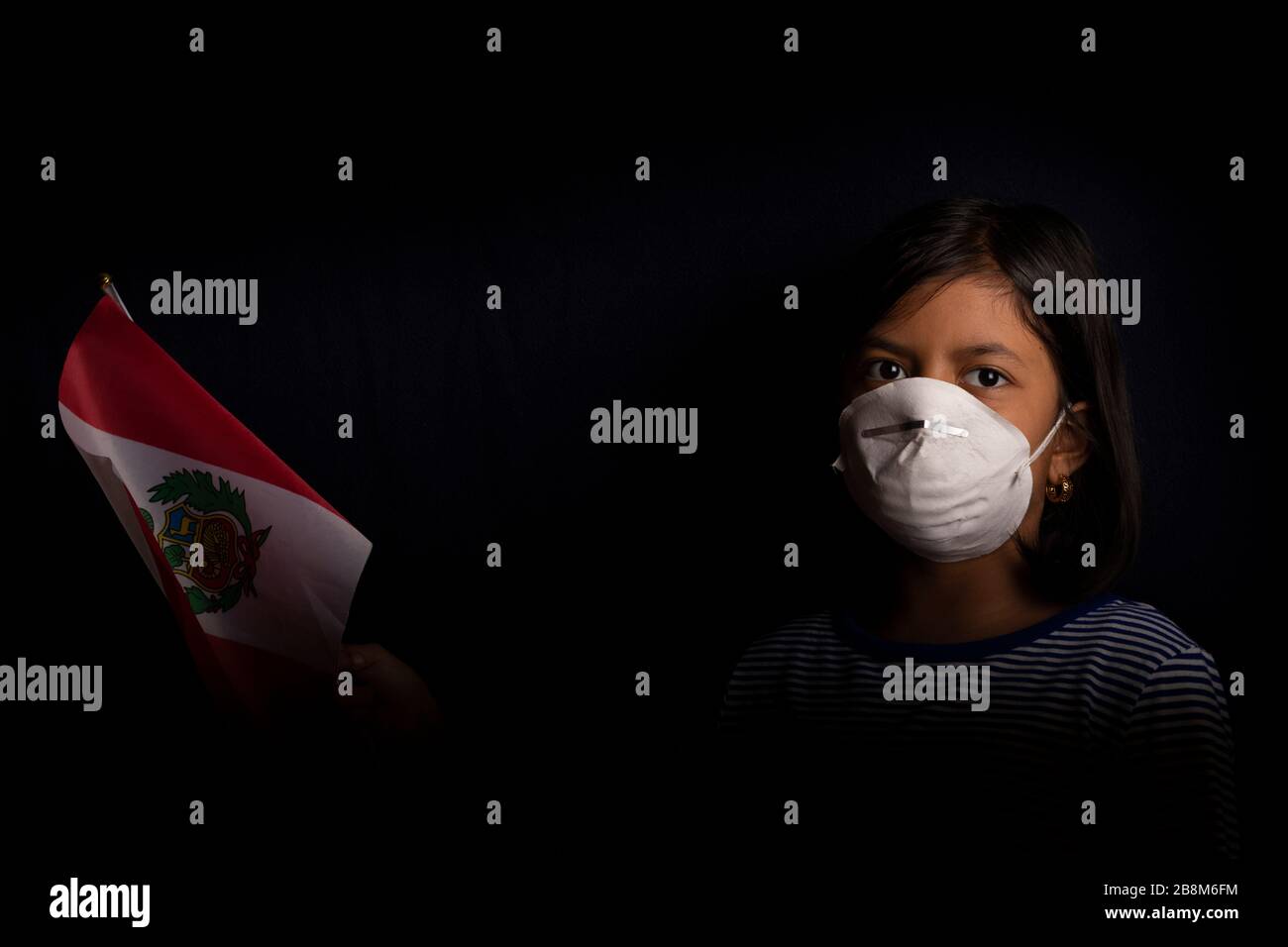 Porträt des kleinen peruanischen Mädchens, das medizinische Maske trägt und hoffentlich die Flagge Perus hält Stockfoto