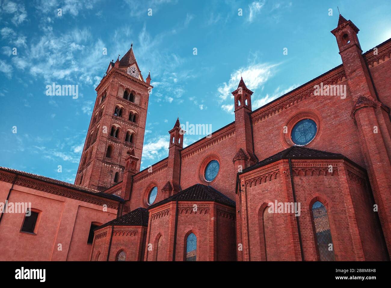 Seitenansicht der Kathedrale San Lorenzo und hoher Belfry unter wunderschönem Himmel mit weißen Wolken in Alba, Piemont, Norditalien. Stockfoto
