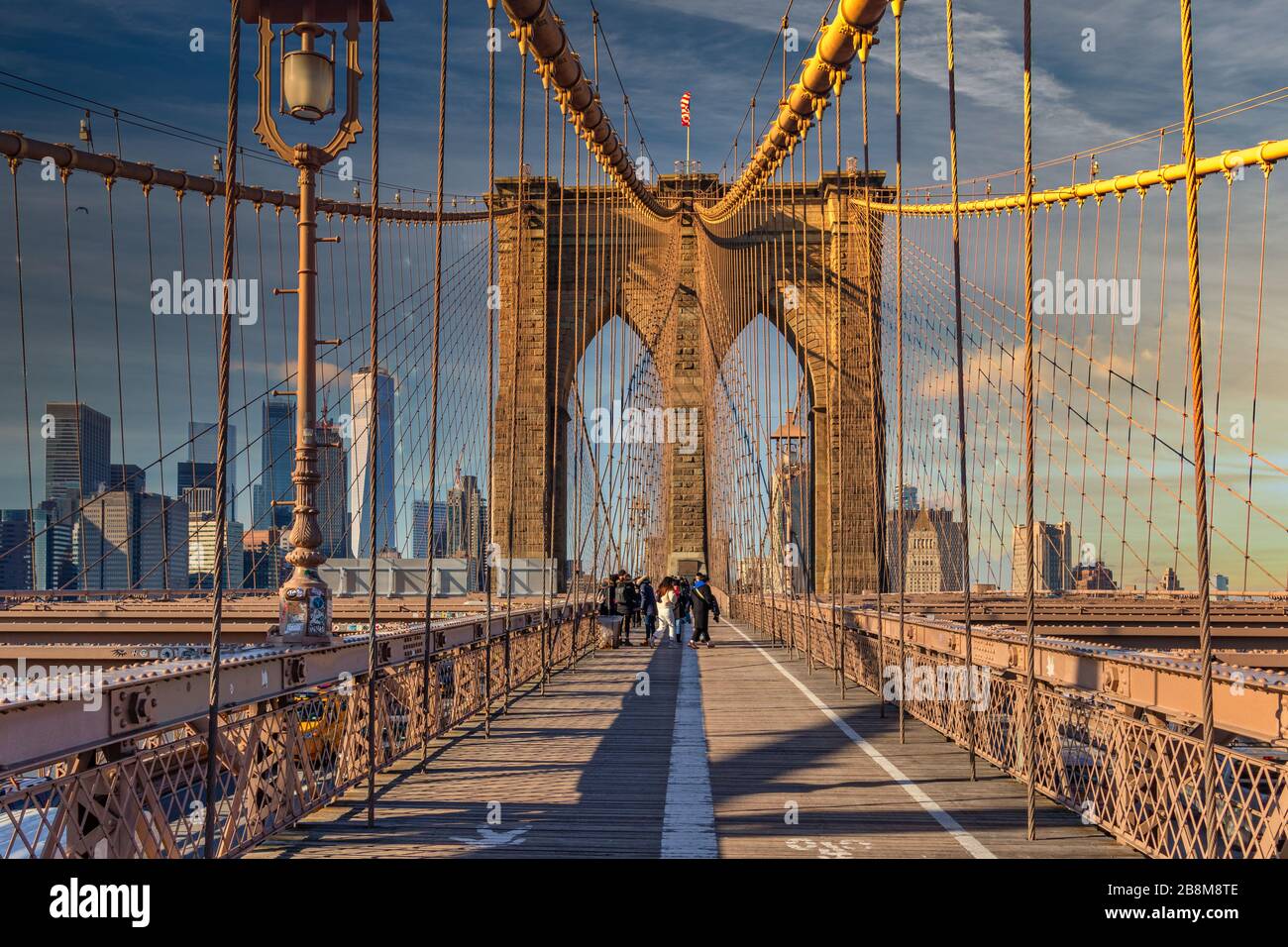 Brooklyn Bridge in NYC Tageslichtansicht mit Menschen zu Fuß, die amerikanische Flagge an der Spitze und Skylines im Hintergrund Stockfoto