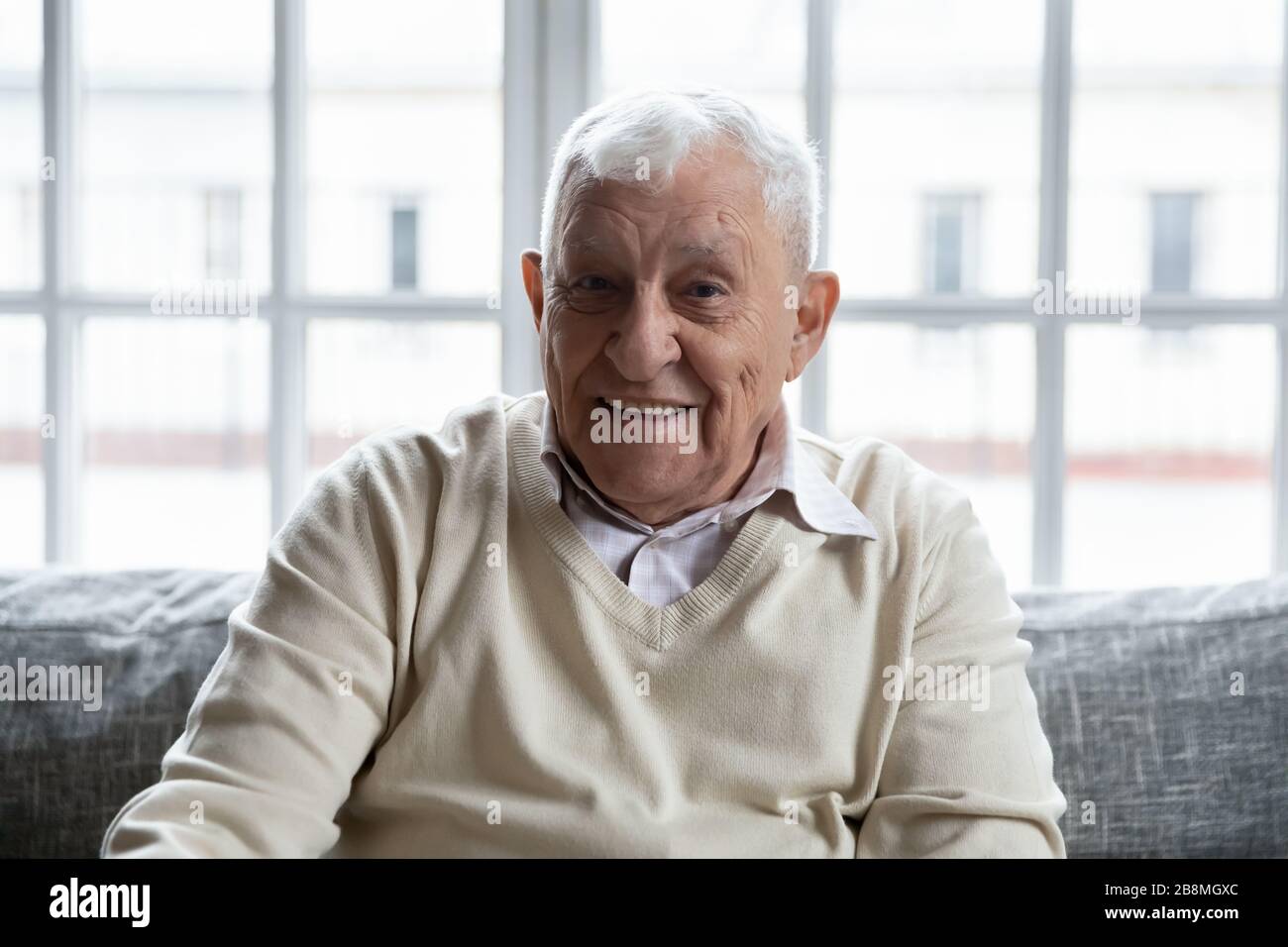 Der alte gesunde positive Großvater sitzt auf der Couch und blickt auf die Kamera Stockfoto