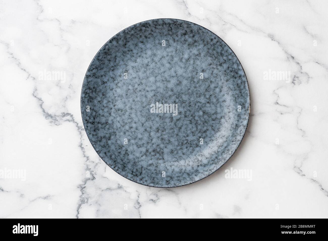 Blaue Platte auf weißem Marmorhintergrund. Leere Platte mit Kopierbereich für Text oder Design. Modernes, modernes Küchenkonzept Stockfoto
