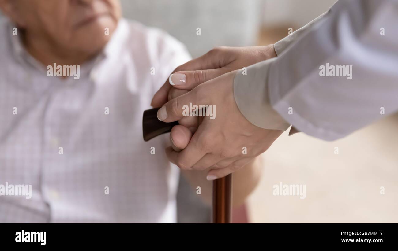 Die Hände des Pflegebedürftigen, die die alten Arme des Patienten halten, berühren den Fußstab in der Nähe Stockfoto