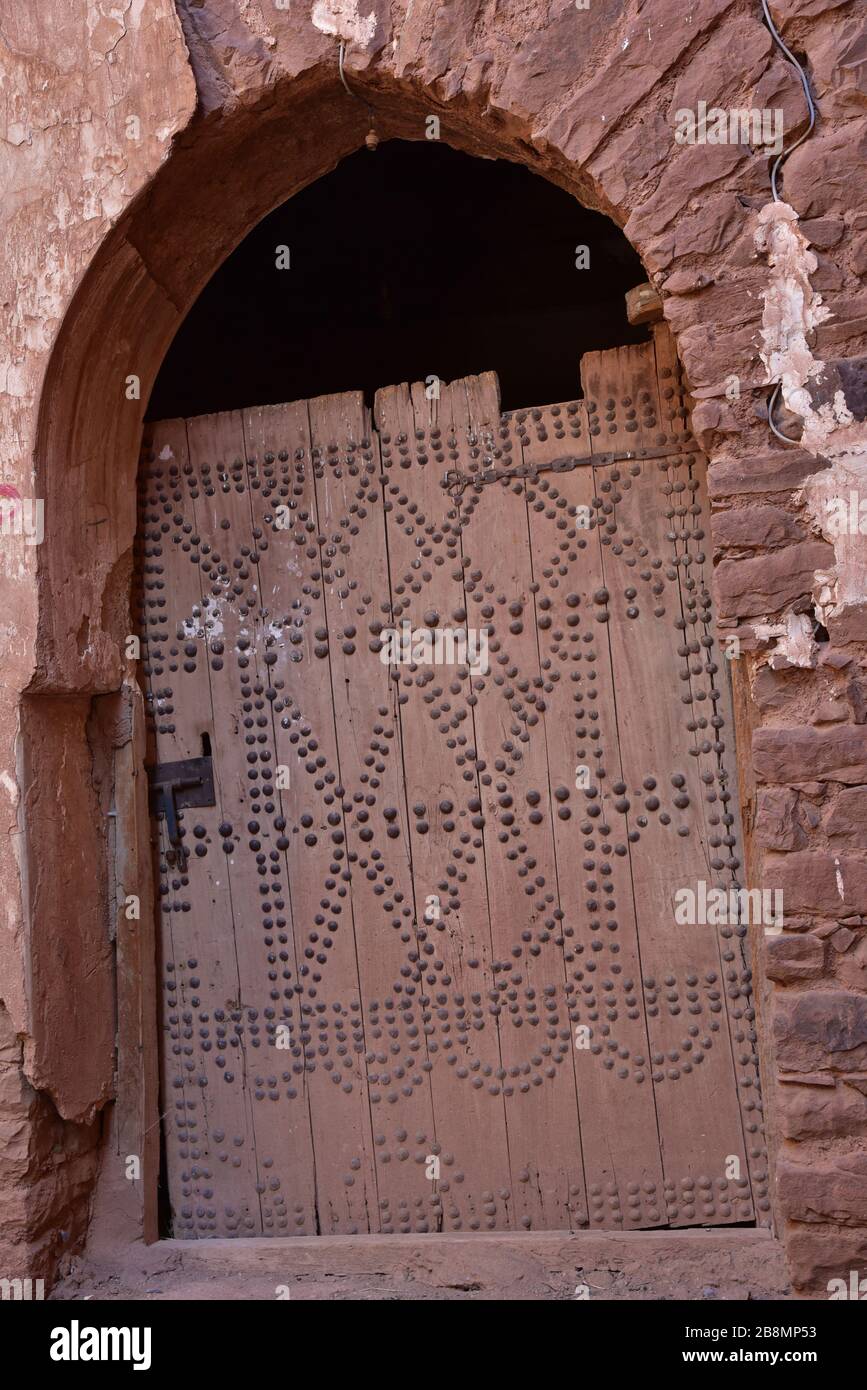 Gealterte, beschlagene Tür mit Nieten, die früher eine traditionelle arabische Tür mit Bogengewölben abschließt, Marokko, Nordafrika. Stockfoto