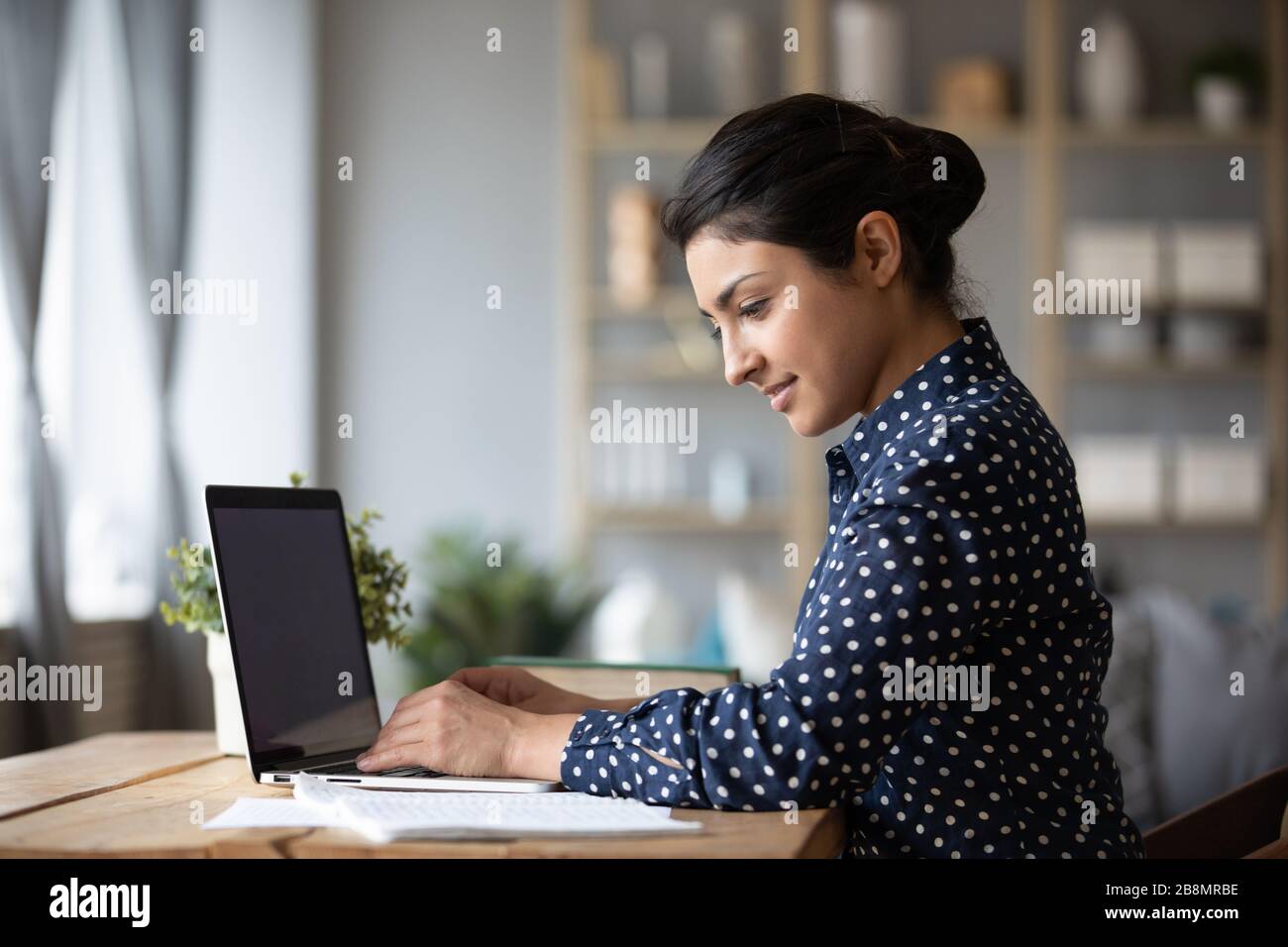Lächelnde Indianerin, die am Laptop arbeitet und Dokumente liest Stockfoto