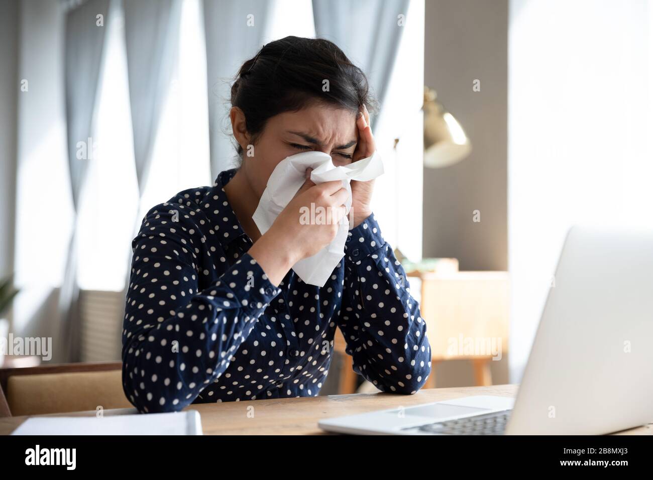 Ungesunde indische Frau bläst die Nase und sitzt am Arbeitsplatz Stockfoto
