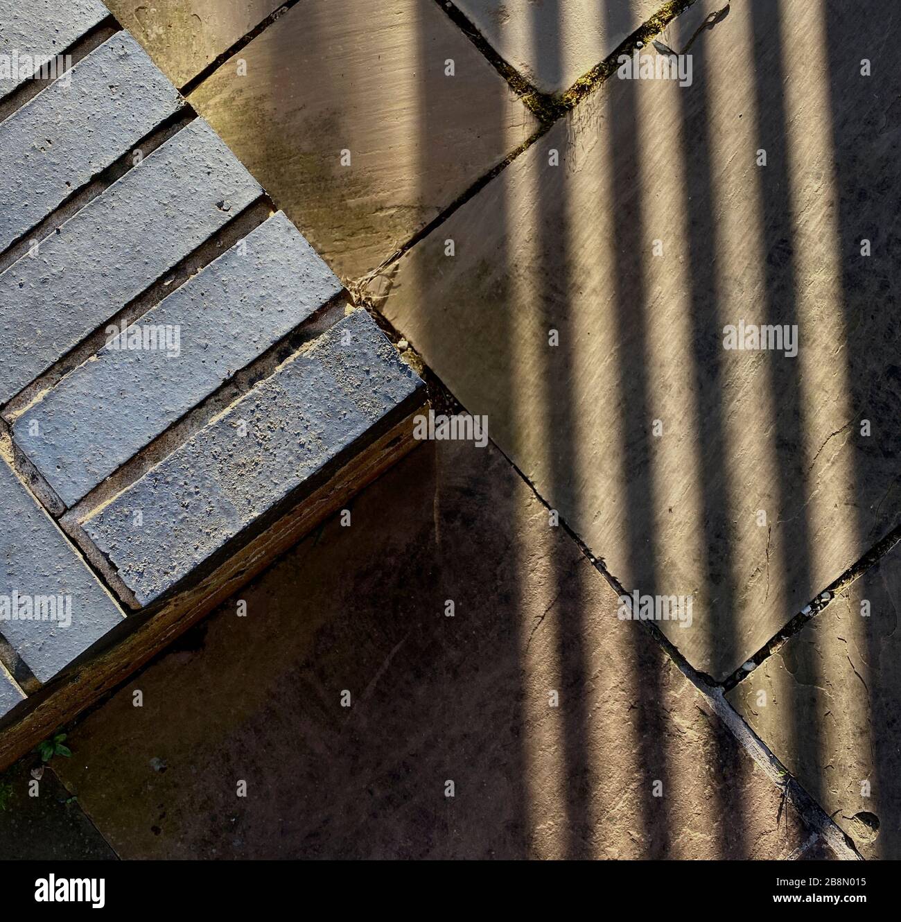 Sonnenschein wirft einen Schatten der Geländer auf eine gepflasterte Terrasse, die eine Mischung aus Mustern und Formen schafft. Stockfoto