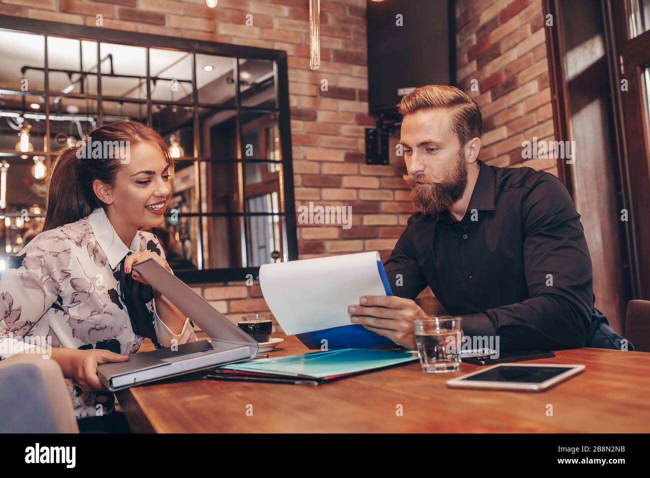 Junge Geschäftsleute arbeiten an Papierarbeiten zusammen und sprechen über Berichte und Finanzen. Porträt des jungen Geschäftsmannes und der Frau, die in Café A sitzen Stockfoto