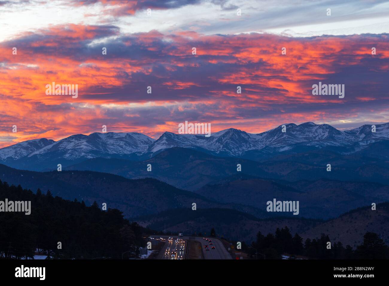 Die Fahrzeuge fahren auf der I-70, während der Sonnenuntergang über den Bergen der Front Range von Colorado drappt Stockfoto